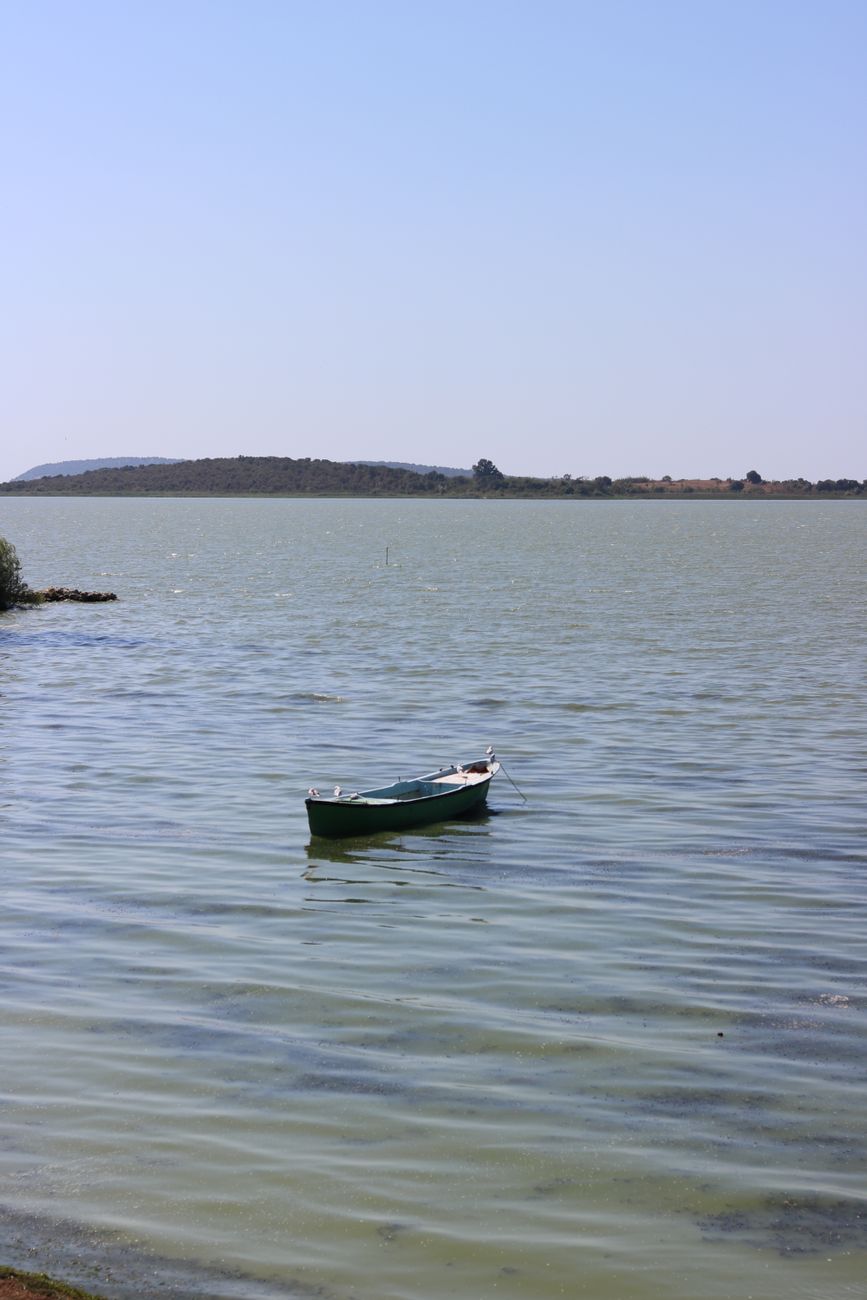 Tranquil scene of a solitary boat floating on a calm lake under a clear sky, evoking peace and solitude.